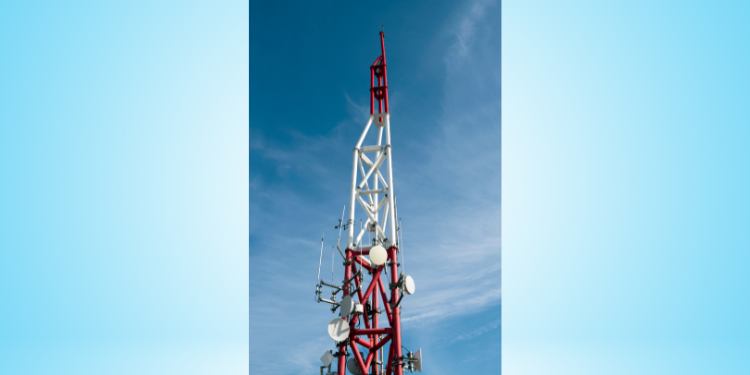 Red and white broadcast transmission tower with multiple antennas and satellite dishes against a blue sky.