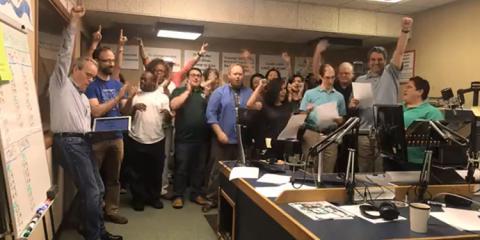Large group of station staff celebrates and cheers when exceeding their programming goals. 
